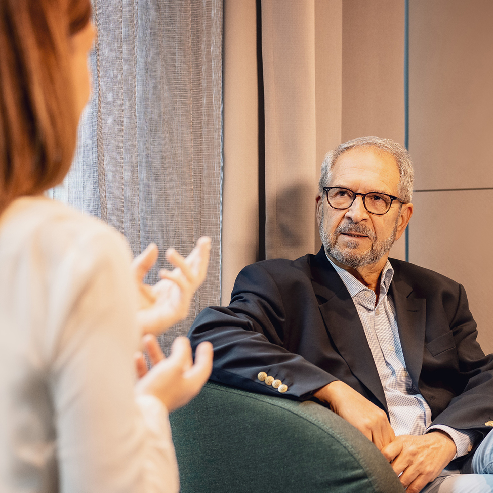 Ein Mann im Anzug, der auf einem Stuhl sitzt, mit einer Frau im Hintergrund